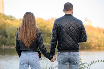 Fototapeta premium Stylish guy and a girl are standing near the river holding hands. Happy husband and wife. Back view.