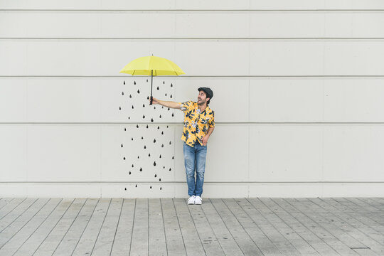 Digital composite of young man holding an umbrella at a wall with raindrops