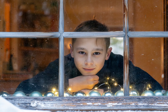 Boy with hand on chin looking through window while sitting at home during Christmas