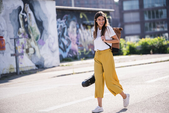 Happy young woman carrying violin case walking on the street