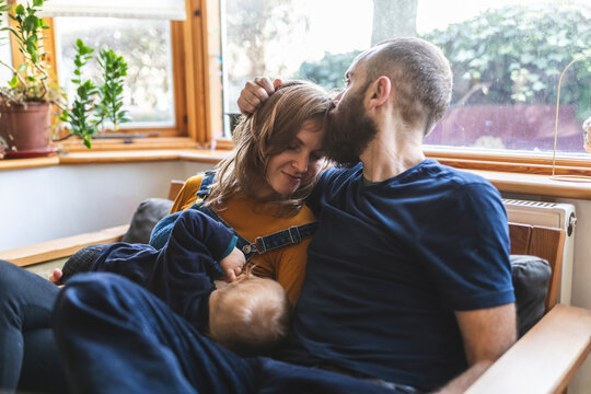 Woman on the sofa breastfeeding her little son and sharing time with her husband