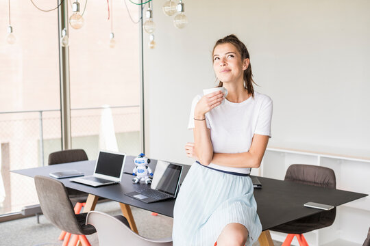 Young businesswoman having coffee break in office looking up