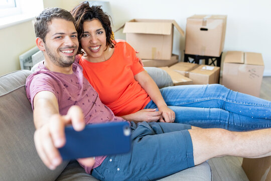 Happy couple taking a selfie on couch in new home