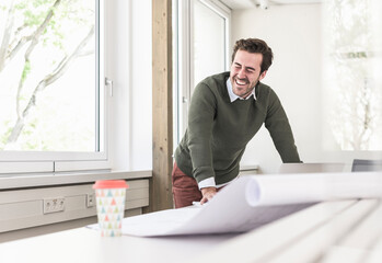 Laughing young architect working on blueprint in bright office