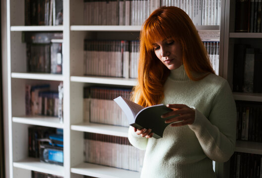 Concentrate woman reading book against shelf at library