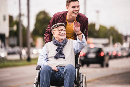 Portrait of laughing young man pushing happy senior man in wheelchair