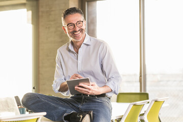 Happy mature businessman with tablet in office
