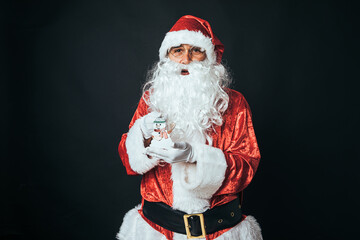 Man dressed as Santa Claus holding a small snowman, on black background. Christmas concept, Santa Claus, gifts, celebration.