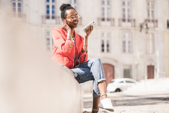 Smiling young woman with earphones and smartphone in the city, Lisbon, Portugal