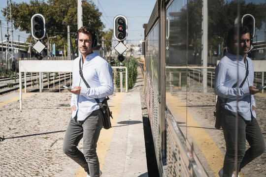 Young man with headphones and smartphone leaving train
