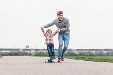Father and son having fun, playing with skateboard outdoors
