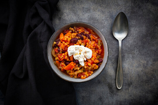 Bowl of vegetarian chili with red lentils, kidney beans, tomatoes, carrots, celery and sour cream
