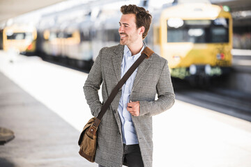 Smiling young businessman at the train station looking around