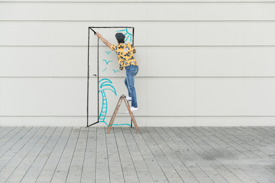 Digital composite of young man drawing a beach at a wall