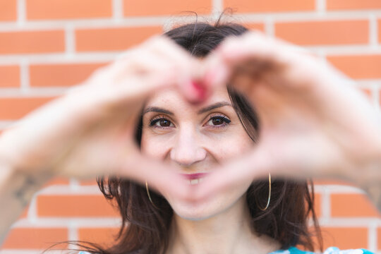 Portrait of smiling young woman looking at camera through heart-shaped hands