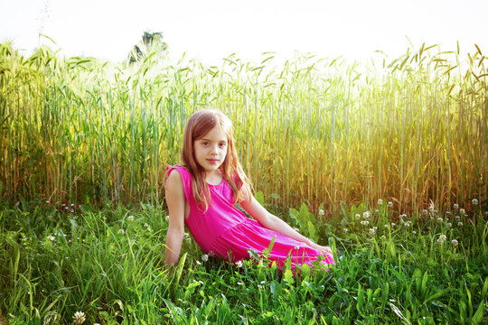 Portrait of young girl wearing vibrant pink dress sitting in front of rye field in summer