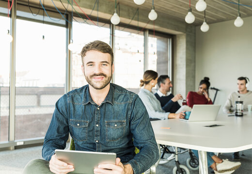 Portrait of smiling young businessman with tablet during a meeting in office