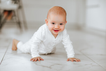 Newborn baby girl in white body growling on white warm floor at home