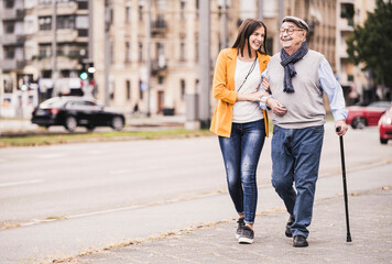 Adult granddaughter assisting her grandfather strolling with walking stick