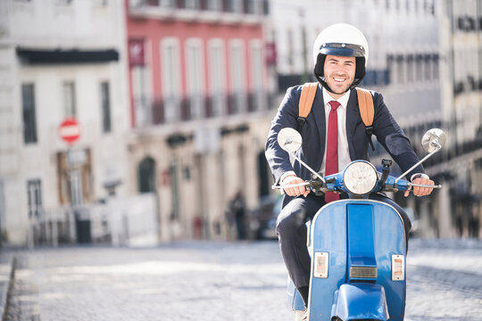 Portrait Of Smiling Young Businessman Riding Motor Scooter In The City, Lisbon, Portugal