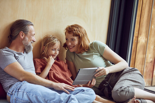 Smiling parents with daughter using digital tablet while relaxing on bed at home