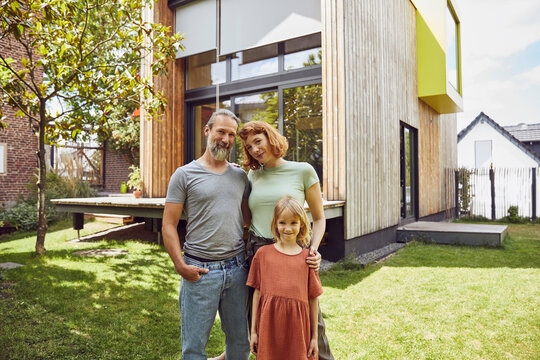 Smiling parents with daughter standing against tiny house in yard