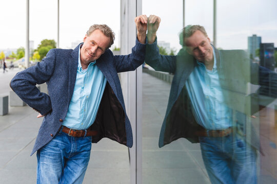 Portrait of confident senior businessman leaning against glass front