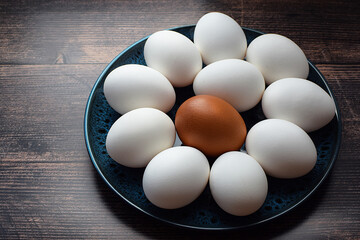 White raw eggs and one brown egg in a bowl on a rustic wooden table. Top and side view. Farm products concept. healthy breakfast.