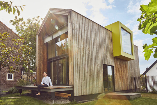 Mature man sitting outside tiny house in yard during sunny day