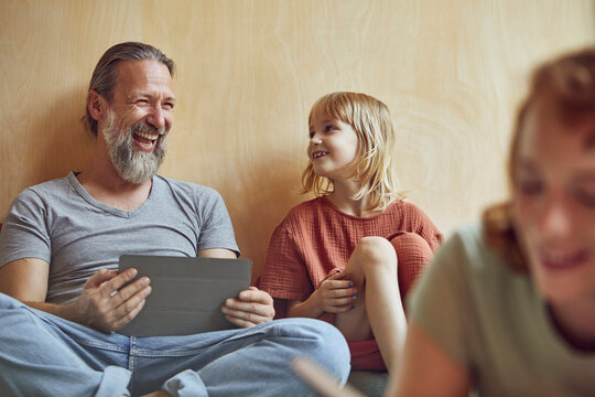 Cheerful father and daughter sitting against wall at home