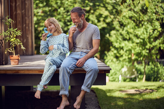 Father and daughter brushing teeth while sitting in yard