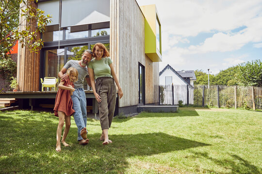 Cheerful parents with daughter standing against tiny house in yard