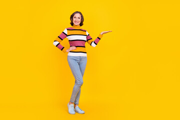 Full length photo of funny grey hairdo old lady hold ad wear striped sweater jeans sneakers isolated on yellow color background