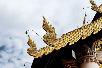 Low angle view of the roof gable of Thai temple on white cloudy background, Thai handicraft roof in cloudy day. Cultural Thai wood carving art at the roof of the temple against the sky.