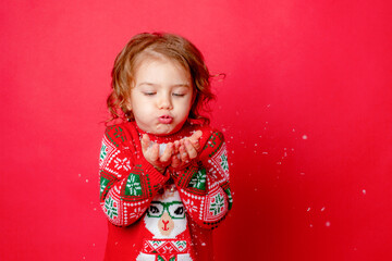 little girl in a sweater with reindeer blowing snow on a red background, christmas, new year