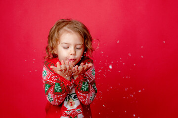 little girl in a sweater with reindeer blowing snow on a red background, christmas, new year