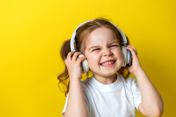portrait of a cute cheerful little girl listening to music with white headphones. audiobooks, audio lessons. concept of education. photo studio, yellow background, text space. High quality photo