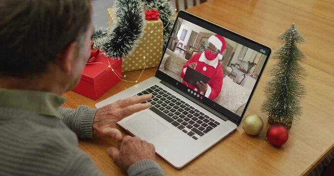 Happy caucasian senior man on video call with santa claus in face mask at christmas time