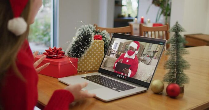 Happy caucasian woman on video call with santa claus in face mask at christmas time