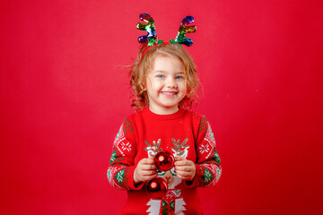 Cute little girl in a red sweater with deer horns on a red background smiling, Christmas, New Year