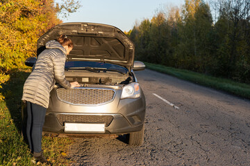 A woman in a jacket is trying to fix a broken car on the road.