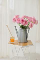 Pink ranunculus in metal watering can with aroma diffuser in interior.