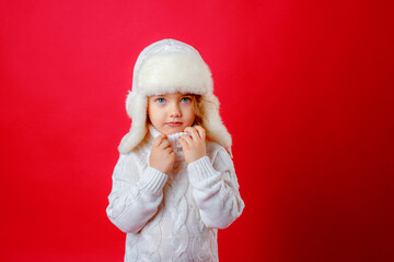 a little girl in a winter hat on a red background smiles