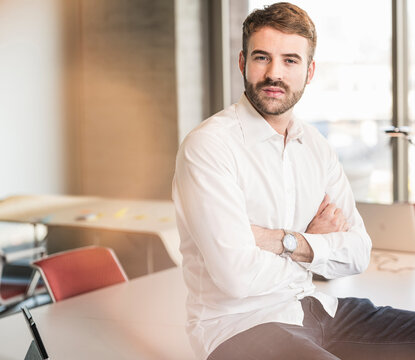 Portrait of a confident young businessman sitting on conference table in office