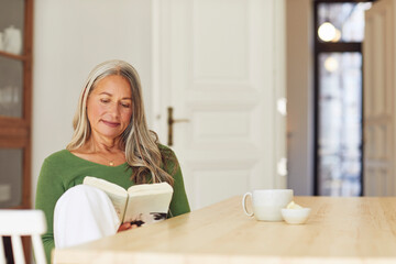 Woman reading book while sitting by table at home
