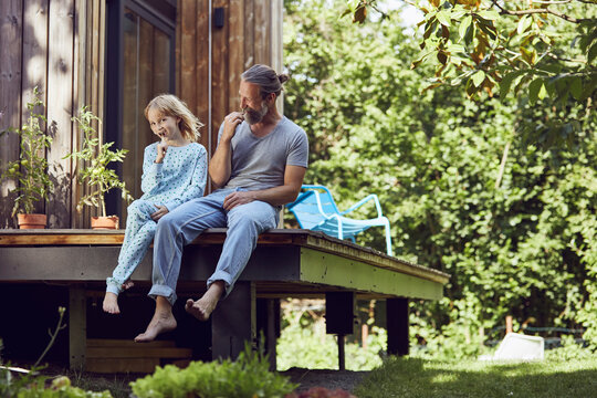 Father and daughter brushing teeth while sitting outside tiny house