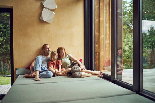 Parents with daughter looking through window while relaxing on bed at home