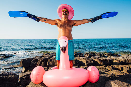 Cheerful man wearing diving flipper in hand while standing on flamingo ring against clear sky