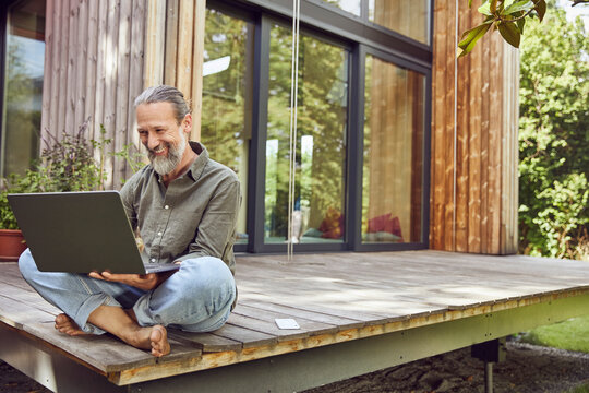 Bearded mature man using laptop while sitting outside tiny house