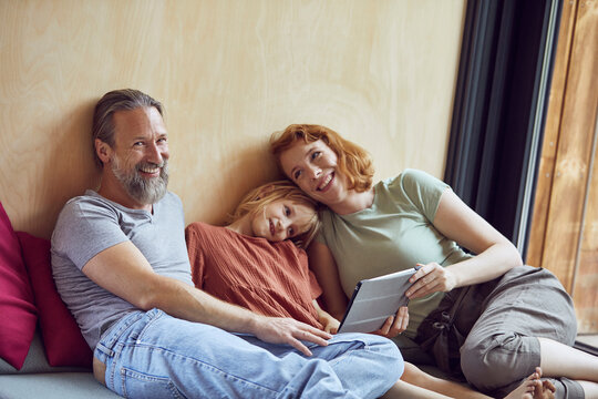 Smiling parents with daughter using digital tablet while lying on bed at home
